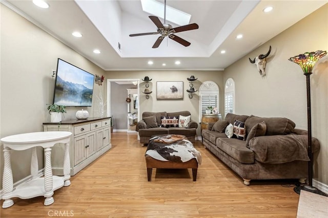 living room featuring a raised ceiling, ceiling fan, light hardwood / wood-style floors, and ornamental molding