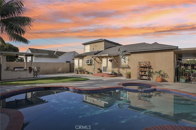 pool at dusk featuring an in ground hot tub and a patio area