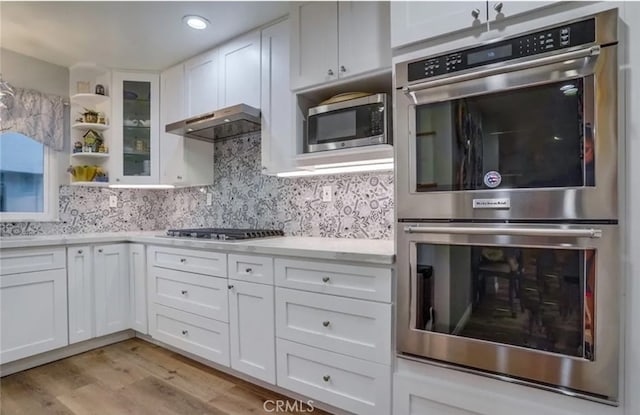 kitchen with light wood-type flooring, white cabinetry, stainless steel appliances, decorative backsplash, and exhaust hood