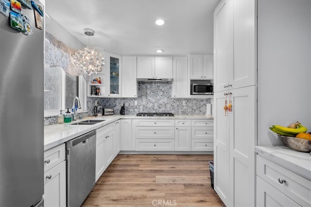 kitchen with hanging light fixtures, appliances with stainless steel finishes, white cabinetry, light hardwood / wood-style flooring, and sink