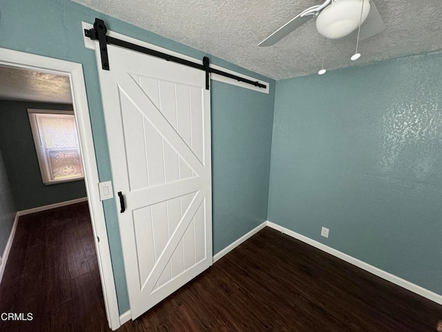 unfurnished bedroom with a textured ceiling, a barn door, dark hardwood / wood-style floors, and ceiling fan