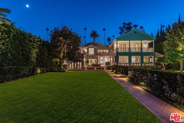 back house at twilight featuring a lawn and a balcony