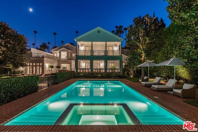 pool at night featuring an in ground hot tub