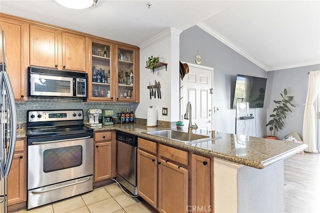 kitchen with appliances with stainless steel finishes, sink, kitchen peninsula, vaulted ceiling, and dark stone countertops