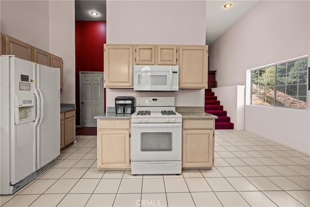 kitchen with light brown cabinets, white appliances, a towering ceiling, and light tile patterned floors