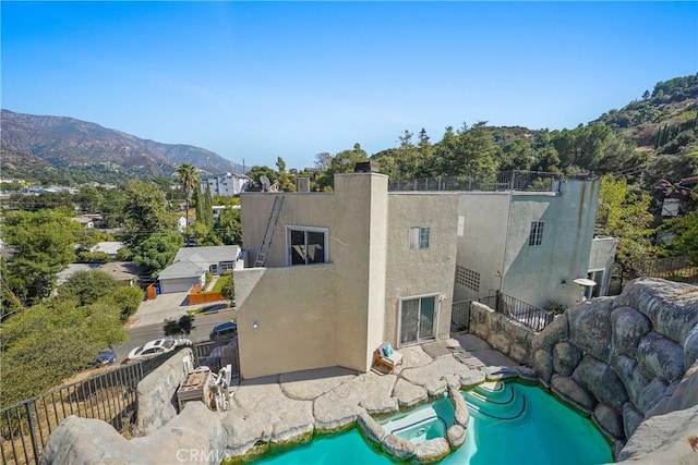 rear view of property featuring a mountain view, a patio area, and a pool with hot tub