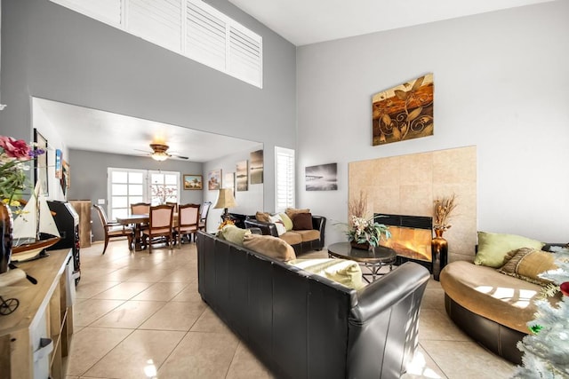 living room with light tile patterned flooring, a towering ceiling, ceiling fan, and a tile fireplace