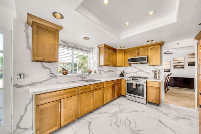 kitchen with a raised ceiling, sink, backsplash, stainless steel appliances, and light stone countertops