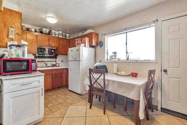 kitchen with decorative backsplash, light tile patterned floors, white fridge, and sink