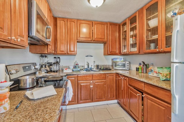 kitchen with light stone countertops, sink, a textured ceiling, light tile patterned flooring, and appliances with stainless steel finishes