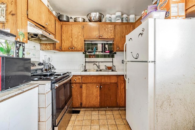 kitchen featuring tasteful backsplash, sink, light tile patterned floors, white fridge, and stainless steel electric range