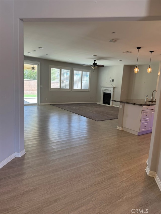 unfurnished living room featuring light hardwood / wood-style floors, sink, and ceiling fan