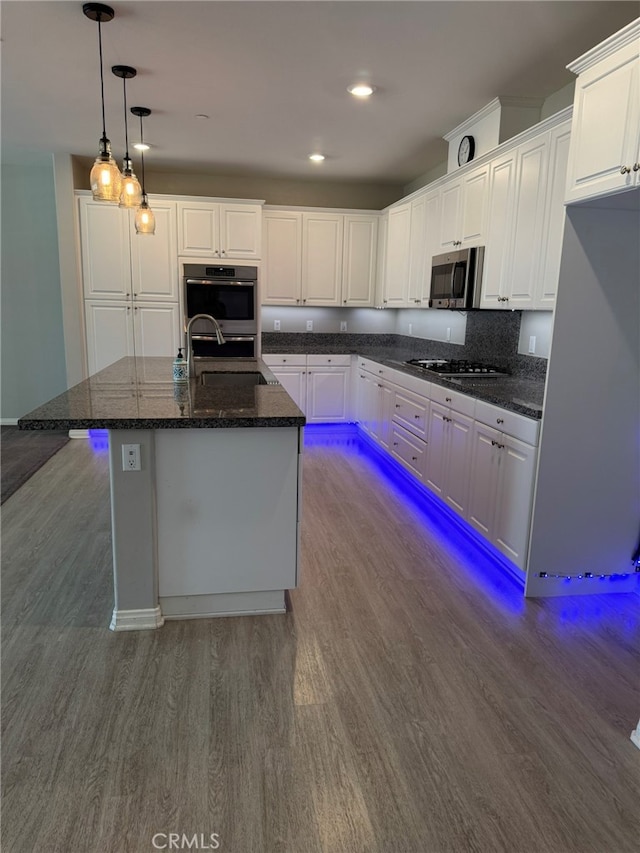 kitchen featuring dark hardwood / wood-style flooring, pendant lighting, dark stone counters, white cabinetry, and a center island with sink