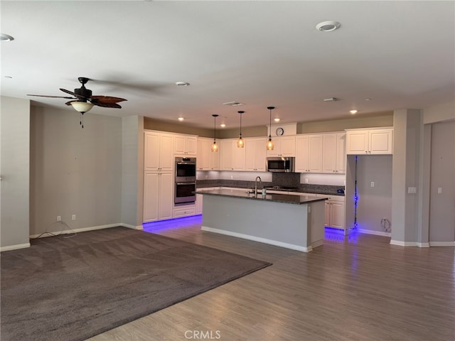 kitchen with dark hardwood / wood-style floors, white cabinets, appliances with stainless steel finishes, decorative light fixtures, and a center island with sink