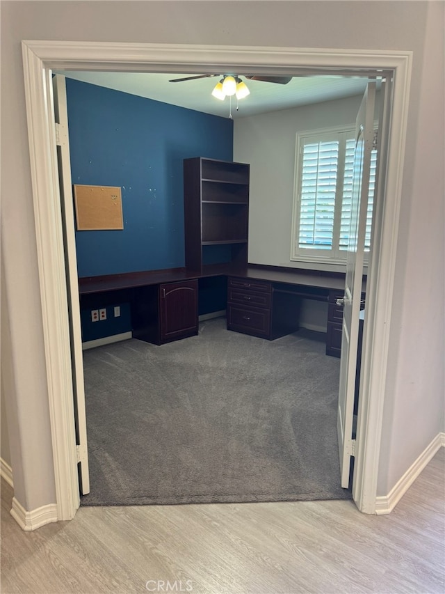 unfurnished office featuring ceiling fan, hardwood / wood-style floors, and built in desk