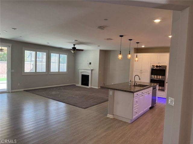 kitchen with white cabinets, sink, a kitchen island with sink, stainless steel appliances, and light wood-type flooring