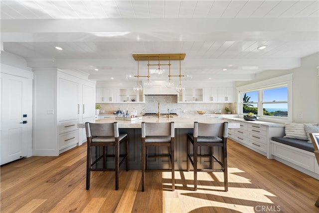 kitchen featuring a breakfast bar, white cabinets, a spacious island, light hardwood / wood-style flooring, and beamed ceiling