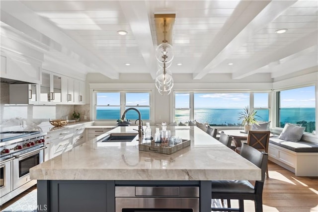 kitchen featuring light stone countertops, a water view, a spacious island, and sink