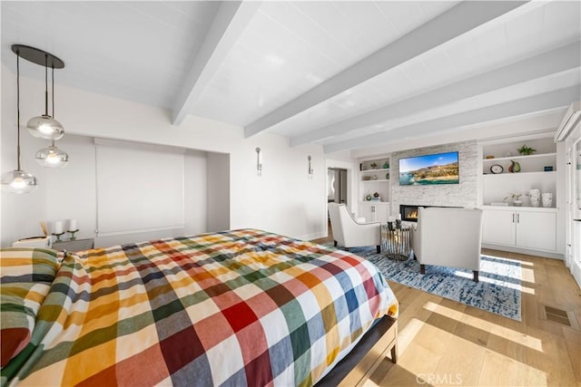 bedroom with beamed ceiling, light wood-type flooring, and a fireplace