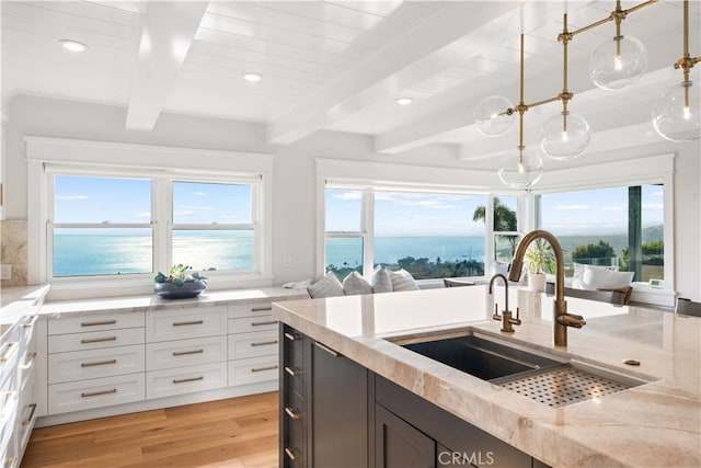 kitchen with light stone counters, decorative light fixtures, a water view, white cabinets, and light wood-type flooring