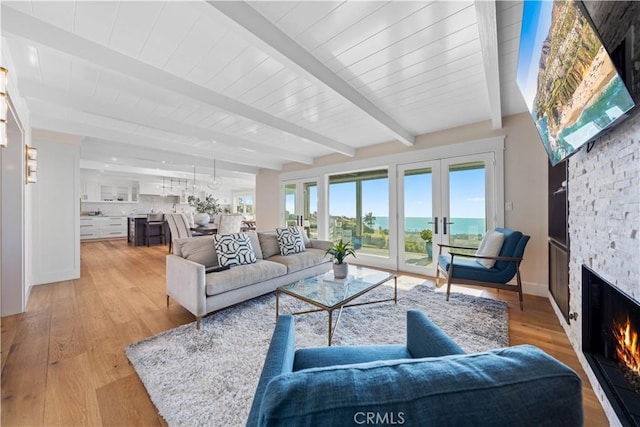 living room with beam ceiling, a stone fireplace, light wood-type flooring, and a water view