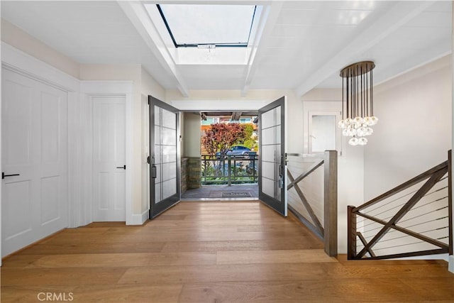 foyer entrance featuring french doors, a skylight, beam ceiling, wood-type flooring, and an inviting chandelier