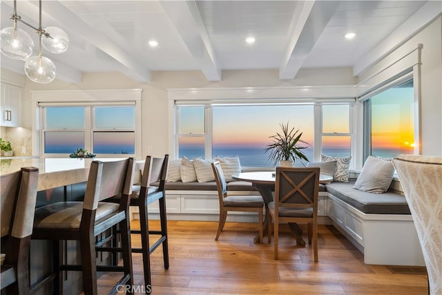 dining space with beam ceiling, breakfast area, a water view, and light hardwood / wood-style flooring