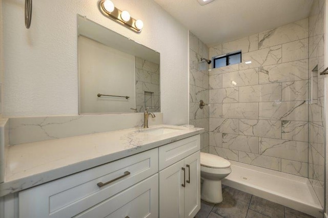 bathroom with toilet, vanity, tile patterned floors, and tiled shower