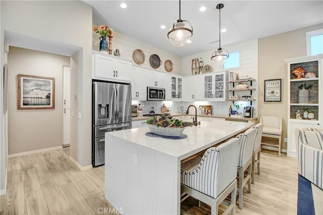 kitchen with tasteful backsplash, white cabinetry, hanging light fixtures, a kitchen island with sink, and stainless steel appliances