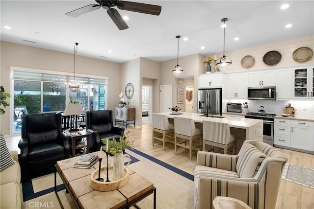 living room with light wood-type flooring, ceiling fan with notable chandelier, and sink