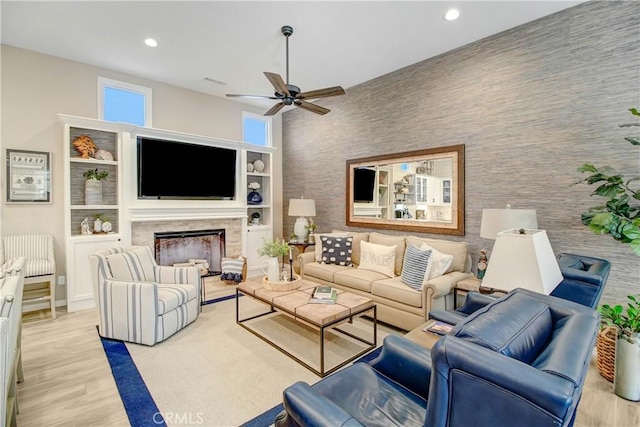 living room featuring ceiling fan, a fireplace, light hardwood / wood-style floors, a towering ceiling, and built in features