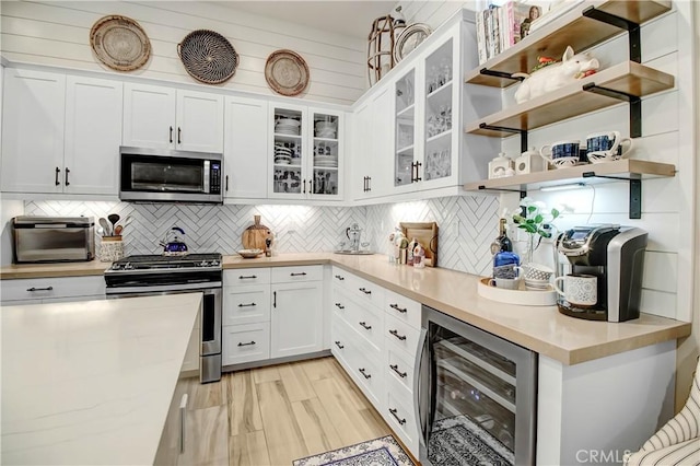 kitchen with white cabinets, stainless steel appliances, tasteful backsplash, wine cooler, and light wood-type flooring