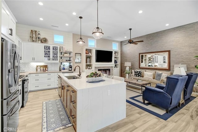 kitchen with appliances with stainless steel finishes, a kitchen island with sink, hanging light fixtures, white cabinets, and sink