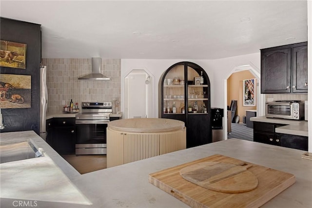 kitchen with dark brown cabinetry, decorative backsplash, electric range, and wall chimney range hood