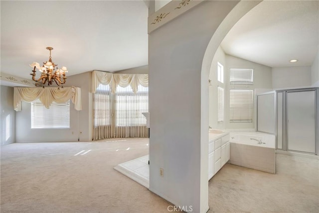 bathroom with tiled tub, vanity, vaulted ceiling, and a chandelier