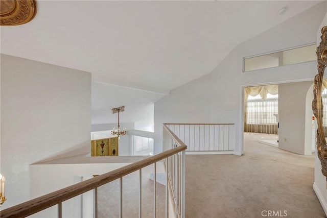 hall with a chandelier, vaulted ceiling, carpet flooring, and an upstairs landing