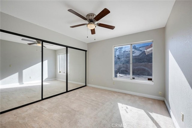 unfurnished bedroom featuring light carpet, ceiling fan, baseboards, and a closet