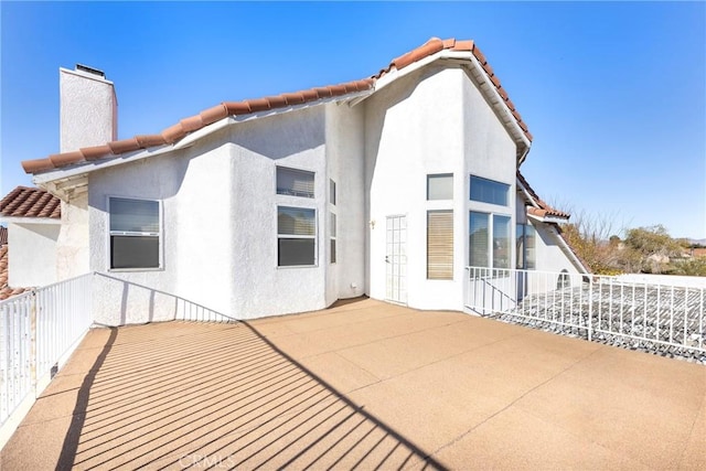 rear view of property with a tile roof, a chimney, and stucco siding