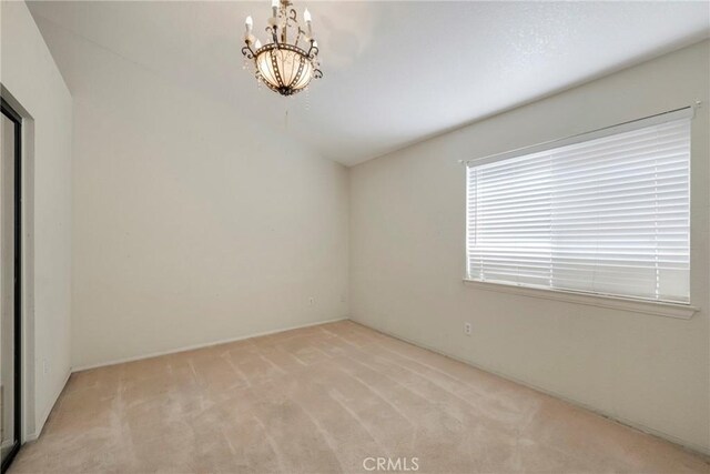 spare room featuring light colored carpet and a notable chandelier