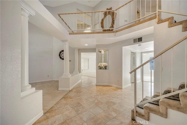 entryway featuring stairway, baseboards, a towering ceiling, and ornate columns