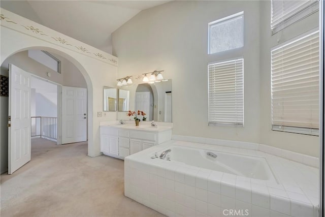 bathroom featuring lofted ceiling, vanity, and tiled bath