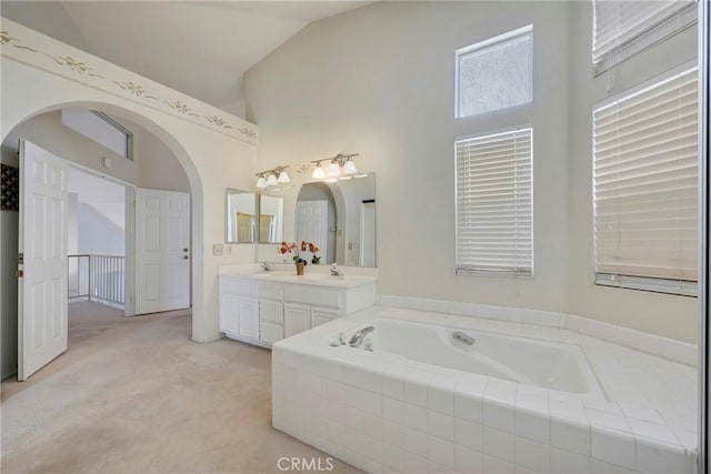 bathroom with double vanity, a garden tub, high vaulted ceiling, and a sink