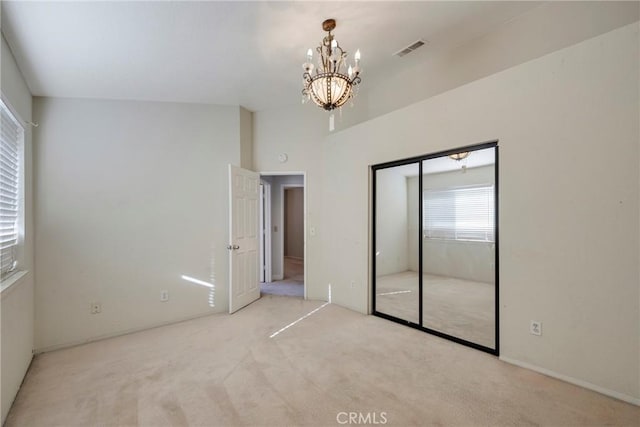 unfurnished bedroom with an inviting chandelier, light colored carpet, lofted ceiling, and a closet