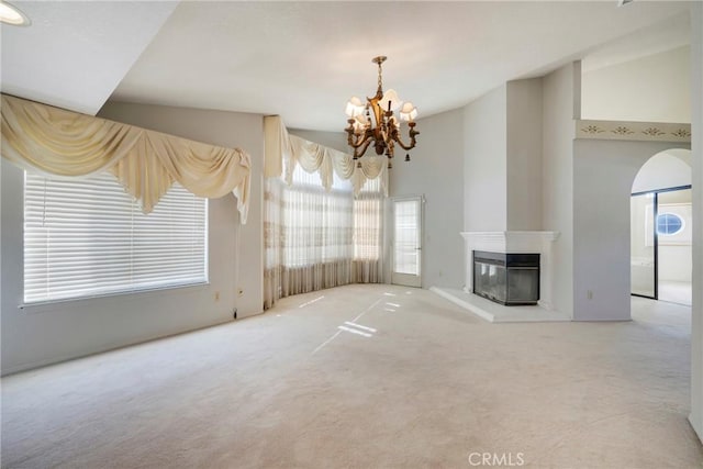 unfurnished living room featuring high vaulted ceiling, a glass covered fireplace, carpet flooring, and a notable chandelier