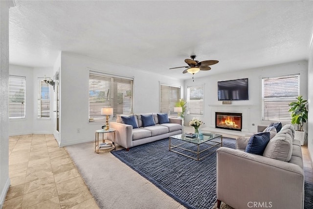 living room featuring light tile patterned floors, a glass covered fireplace, ceiling fan, a textured ceiling, and baseboards