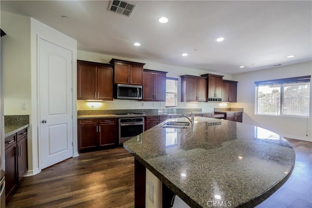 kitchen with a center island with sink, dark hardwood / wood-style floors, dark stone countertops, and stainless steel appliances