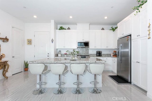 kitchen featuring white cabinetry, a kitchen island with sink, light stone countertops, and appliances with stainless steel finishes