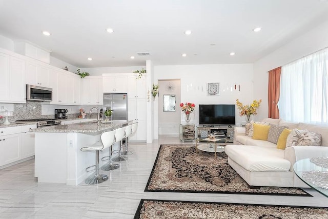 kitchen with white cabinets, appliances with stainless steel finishes, a center island with sink, and a kitchen breakfast bar