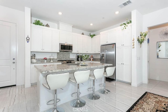 kitchen with a breakfast bar area, white cabinetry, an island with sink, and appliances with stainless steel finishes