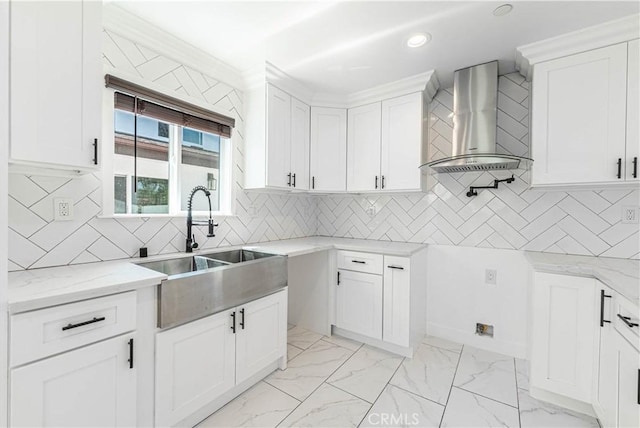 kitchen with tasteful backsplash, light stone counters, wall chimney exhaust hood, sink, and white cabinetry